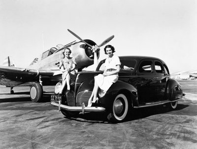 Kalifornie: 1939 Dvě ženy sedí na blatnících sedanu Lincoln Zephyr z roku 1939 na letišti s jednomotorovým letadlem zaparkovaným za nimi (černobílá fotografie) od Unbekannt