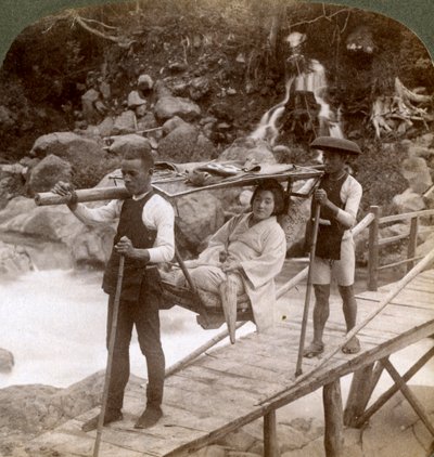 Japonka v horském křesle yamakago překračující přívalovou řeku Daiya poblíž Nikko, Japonsko, od Underwood and Underwood