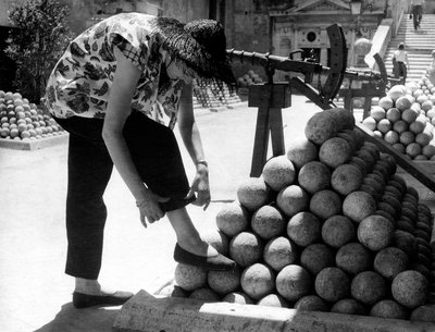 Žena si upravuje manžetu u kalhot a opírá si nohu o hromadu dělových koulí v areálu Andělského hradu v Římě. od Unknown photographer