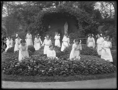 Maturitní ročník dívek z římskokatolického sirotčince v květinové zahradě před jeskyní Panny Marie, 1912 čb fotografie od William Davis Hassler