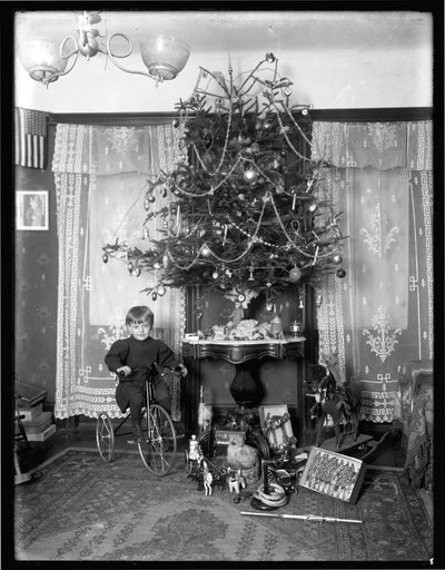Seymour chlapec pózoval sedící na tříkolce vedle vánočního stromku v salonu, Vánoce 1912 od William Davis Hassler