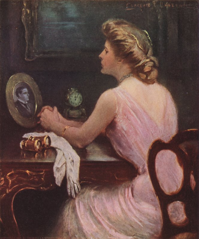 Žena sedí u svého toaletního stolku a dívá se na fotografii muže, možná jejího manžela nebo milence od Clarence F. Underwood