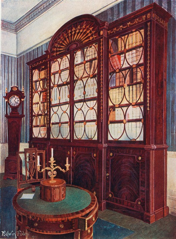 Přední vykládaná mahagonová knihovna. Středový stůl s mahagonovým podstavecem. Hodiny s vysokým pouzdrem z mahagonu od Edwin John Foley