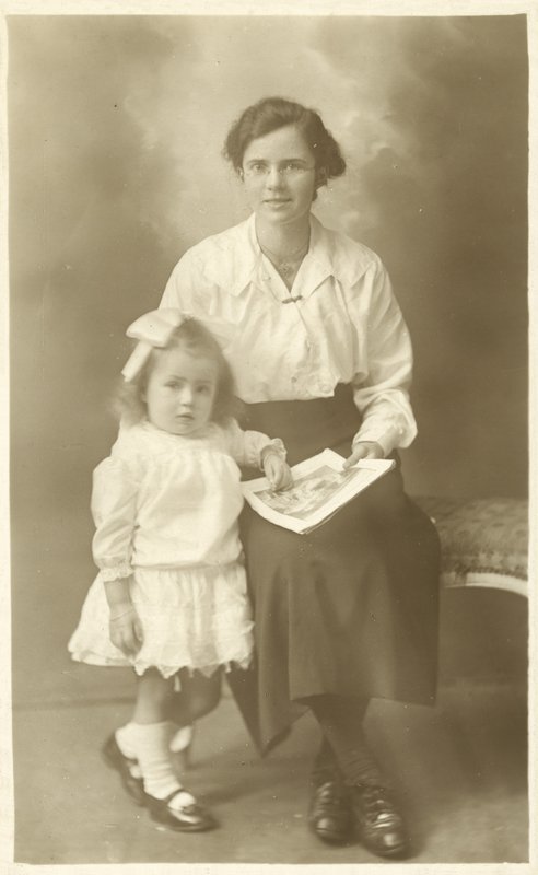 Hezká dívka, matka nebo vychovatelka, ukazuje fotky malému dítěti (černobílá fotografie) od English Photographer