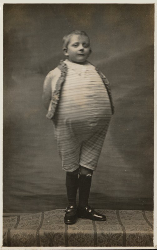Školák, oblečený tak, aby měl velmi velké břicho (černobílá fotografie) od English Photographer