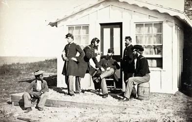 Pět vojáků občanské války se shromáždilo na hliněné verandě před domem, poblíž nich seděla afroamerická mládež, 1861-65