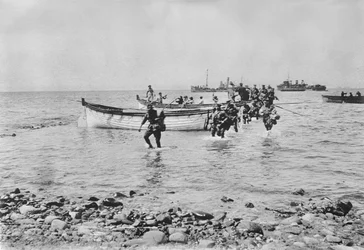 Australští vojáci brodící se vodou, když 25. dubna 1915 vystoupili na břeh v Anzac Cove v Gallipoli poté, co byli přepraveni na vyloďovacích člunech z větších lodí v pozadí, 25. dubna 1915 (