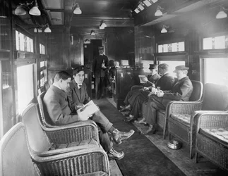 Skupina mužů cestujících v bufetovém voze knihovny ve vlaku Deluxe Overland Limited, USA, cca 1915 (černobílá fotografie)