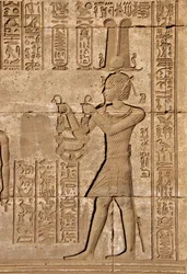 Egyptský starověk: Římské mammisi připomínající narození Ihyho, syna Isis - Detail reliéfů a hieroglyfů: Císař Trajan nesoucí obětiny bohyni Hathor - Chrám Hathor, Denderah, Egypt - Egyptská civilizace: Císař Trajan nesoucí