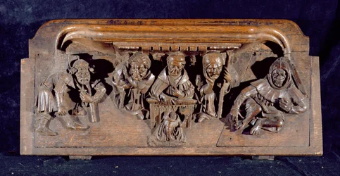 Misericord zobrazující akademika sedícího u panelového stolu, který napomíná klečícího kajícníka, New College Chapel, Oxford, konec 14. století (dřevo)