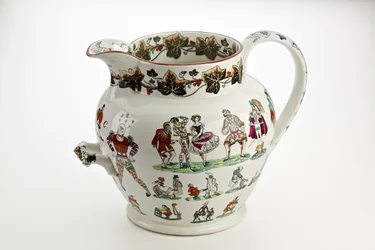 Staffordshire džbán zdobený figurkami Harlekýna a karnevalovým motivem, 1866 (železný porcelán)