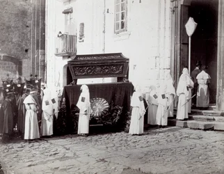 Smuteční průvod kongregace San Francesco v Neapoli. V popředí, před kostelem, doprovázejí četní „bratři z bratrstva“ v bílých tunikách a kápích katafalk zdobený vyšívanou látkou, na které je umístěna rakev.