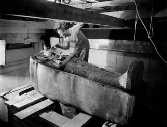 Objev hrobky faraona Tutanchamona v Údolí králů (Egypt): v pohřební komoře Howard Carter pracuje na víku druhé rakve, říjen 1925, fotografie Harryho Burtona (p1568)