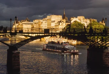 Pod mostem Pont des Arts proplouvá loď a nad hlavou se stahují tmavé mraky. Řeka Seina, Pa...