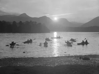 Pohled na lidi plující na kánoích po vodě Derwentwater při východu nebo západu slunce