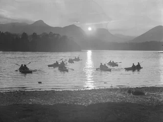Pohled na lidi plující na kánoích po vodě Derwentwater při východu nebo západu slunce