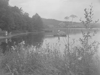 Muž rybařící na člunu na vodě Estwaite Water a dvě dívky na břehu vody