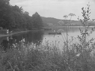 Muž rybařící na člunu na vodě Estwaite Water a dvě dívky na břehu vody