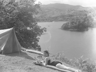 Pohled na mladou ženu v plavkách ležící na lilo, v pozadí jezero.