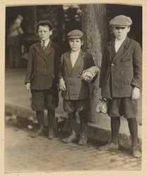 [Tři chlapci na městské ulici v kalhotách a čepicích]