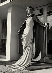 Model ve večerních šatech vytvořený couture house "Graldi". Článek je doplněn pláštěm z lehké tkaniny. (černobílá fotografie)