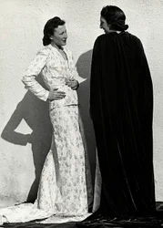Dva modely představují výtvory italského módního domu "Dragoni". Jedna modelka má na sobě outfit z plenkového materiálu skládající se z bundy a dlouhé sukně s vlečkou. Druhý model, při pohledu zezadu, má na sobě dlouhý sametový plášť. (černobílá fotografie