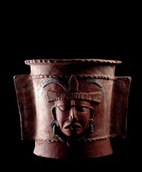 Předkolumbovské umění, mayská civilizace, pozdní klasické období: válcovitá hliněná pohřební urna zdobená lidskou tváří. Z Quiché, Guatemala. Rozměry: výška 38.5 x průměr 39,5 cm. Guatemala, Národní muzeum archeologie a etnologie