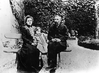 Pierre (1859-1906) a Marie Curie (1867-1934) sedící na lavičce v zahradě.