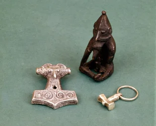 Amulety vikingských božstev: v popředí dvě malá stříbrná kladiva symbolizující boha Thora. Soška představuje Freyra, boha plodnosti. Historické muzeum ve Stockholmu, Švédsko.