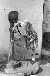 Holčička vyprazdňuje kbelík s vodou v pumpovací fontáně, 9. května 1939 (čb fotografie)