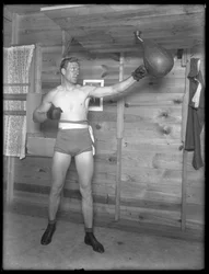 Anglický boxer William Thomas Wells (Bombardier Billy Wells), pózující v tréninkových taškách s taškou na rychlost, kolem roku 1911.