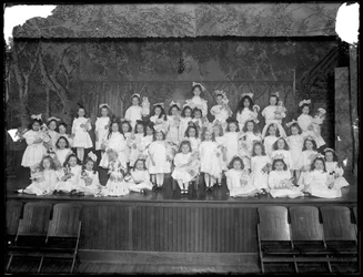 Skupina děvčátek pózujících na malém pódiu a držících panenky, pravděpodobně Roman Catholic Orphan Asylum, Kingsbridge, Bronx, asi 1911