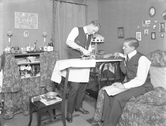 Neznámý muž předvádějící použití elektrické žehličky, sledovaný jiným mužem, kolem roku 1913-14