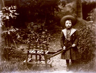Dívka s vozíkem v zahradě, začátek dvacátého století (černobílá fotografie)